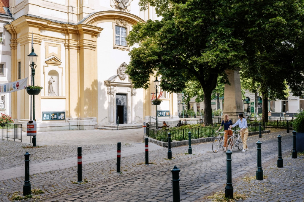 Zwei Passant*innen die plaudernd ihr Fahrrad auf Kopfsteinpflaster schieben